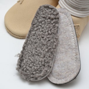 Könnte beinhalten: Zwei Paar Einlegesohlen für Schuhe. Ein Paar ist grau und flauschig, das andere ist beige und glatt.