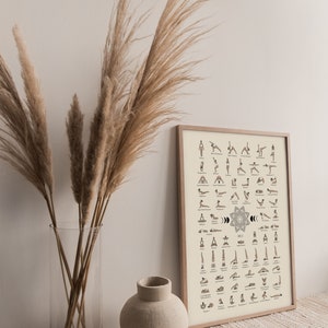 May include: A framed poster with a beige background and black illustrations of yoga poses. The poster is titled "Yoga" and includes the names of each pose. The poster is hanging on a wall with a vase of dried pampas grass in front of it.