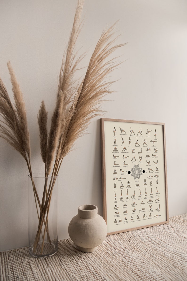 May include: A framed poster with a beige background and black illustrations of yoga poses. The poster is titled "Yoga" and includes the names of each pose. The poster is hanging on a wall with a vase of dried pampas grass in front of it.