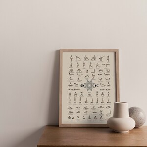 May include: A framed poster with a beige background and illustrations of different yoga poses. The poster is titled "Yoga" and includes the names of each pose. The poster is hanging on a white wall above a wooden dresser with a vase and a stone object on top.