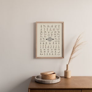 May include: A framed poster with a beige background and black illustrations of yoga poses. The poster is titled "The Way to Samadhi" and includes the text "Est. 2016". The poster is hanging on a light beige wall above a wooden cabinet with a light brown wooden drawer.