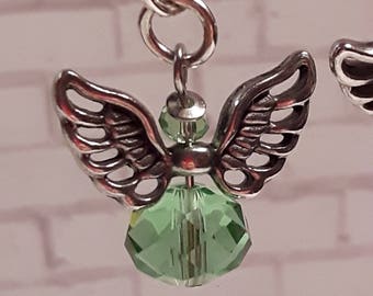 May include: A silver angel charm with a green crystal pendant. The angel has delicate wings and a detailed design. The charm is attached to a silver chain.