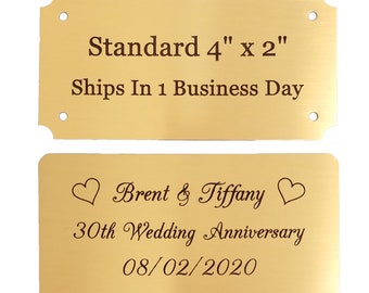 May include: Two gold metal plaques with engraved text. The top plaque reads "Standard 4" x 2" Ships In 1 Business Day". The bottom plaque reads "Brent & Tiffany 30th Wedding Anniversary 08/02/2020" with a heart symbol on each side of the names.
