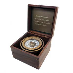 May include: A brass compass with a white face and a black needle is displayed in a wooden box. The box is open and the compass is sitting on a green felt lining. The inside of the box lid has an engraved quote: "So throw off the bowlines, sail away from the safe harbor. Catch the trade winds in your sails. Explore. Dream. Discover."