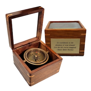May include: A brass compass with a wooden box and a glass lid. The box has a quote by Henry David Thoreau: "Go confidently in the direction of your dreams! Live the life you've imagined."