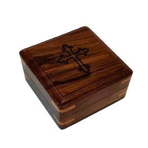 May include: A small wooden box with a cross design on the lid. The box is made of dark wood with a reddish brown hue and has a brass inlay around the edges.