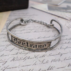 May include: A silver bracelet with a decorative band that reads "Bertrand".
