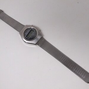 May include: A silver digital watch with a mesh metal band. The watch face displays the time and date.