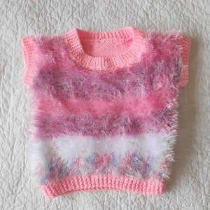 Puede incluir: Un suéter de punto sin mangas de color rosa y morado con una franja blanca.