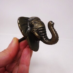 May include: A bronze-colored elephant head hook with a screw on the back. The hook is designed to be used as a wall hook.
