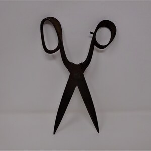 May include: A pair of antique black metal shears with a long handle and a pointed tip. The shears are open and ready to cut.