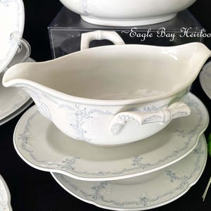 May include: A white porcelain gravy boat with a blue floral design and a handle on each side. The boat is sitting on a white porcelain saucer with a blue floral design. The saucer is sitting on a white porcelain plate with a blue floral design.