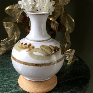 May include: White ceramic vase with brown and tan abstract design. The vase is sitting on a cork coaster on a green marble surface. The text "Eagle Bay Heirlooms" is visible on the surface.