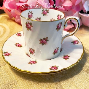 May include: A white teacup and saucer with a gold rim and a pink rose pattern. The text "Eagle Bay Heirlooms" is visible on the saucer.