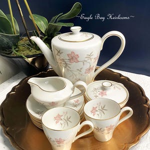 May include: A vintage tea set with a floral design. The set includes a teapot, creamer, sugar bowl, and four cups and saucers. The set is decorated with pink flowers and gold trim.
