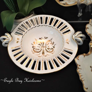 May include: White porcelain serving dish with gold trim and a decorative floral design. The dish has a scalloped edge and two handles.