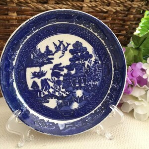 May include: A blue and white porcelain saucer with a willow pattern design. The saucer is on a clear plastic stand.