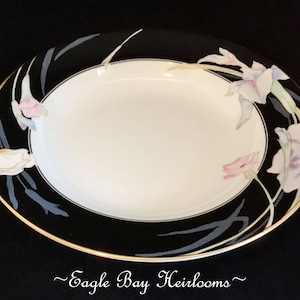 May include: A black and white soup bowl with a gold rim. The bowl features a floral design with pink, purple, and white flowers on a black background. The text "~Eagle Bay Heirlooms~" is printed on the bottom of the bowl.
