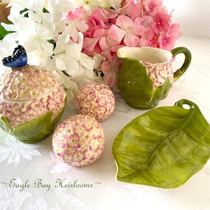 May include: A set of pink and green floral-themed ceramic sugar and creamer set with a matching leaf-shaped serving dish. The sugar bowl has a butterfly on the lid.  The set is decorated with pink and green flowers.