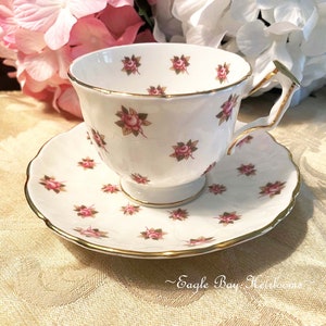 May include: A white teacup and saucer with a delicate pink rose pattern and gold trim. The set is decorated with small pink roses and green leaves.