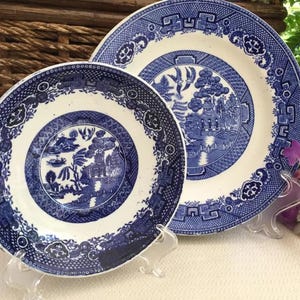 May include: Two blue and white porcelain plates with a willow pattern design. The smaller plate is on top of the larger plate.