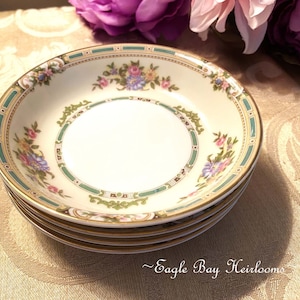 May include: A set of four white porcelain bowls with a green and gold floral design. The bowls are stacked on top of each other.