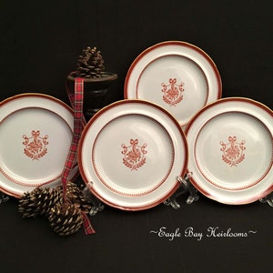 May include: Set of four white ceramic dessert plates with a red and gold trim. Each plate features a red floral design with a bow and a wreath.