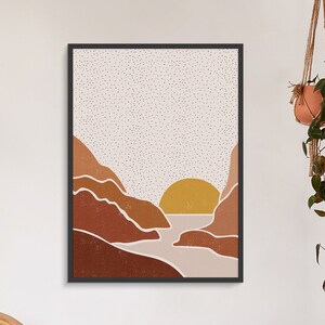 May include: A framed print of a minimalist landscape with a sunset over a body of water. The print features a muted color palette of brown, beige, and yellow.