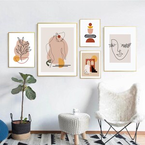 Op de afbeelding: Set van vijf minimalistische line art prints met abstracte vormen en kleuren. De prints tonen een vrouw, een plant, een geometrisch ontwerp, een boog en een gezicht. De prints zijn ingelijst in goud en hangen aan een witte muur.