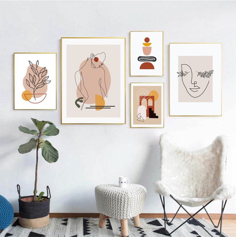 Op de afbeelding: Set van vijf minimalistische line art prints met abstracte vormen en kleuren. De prints tonen een vrouw, een plant, een geometrisch ontwerp, een boog en een gezicht. De prints zijn ingelijst in goud en hangen aan een witte muur.