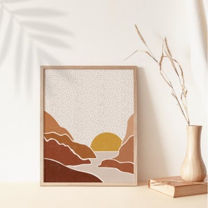 May include: A framed print of a minimalist landscape with a sunset over a body of water. The print features a light brown background with a white dotted pattern, and the landscape is depicted in shades of brown, orange, and yellow.