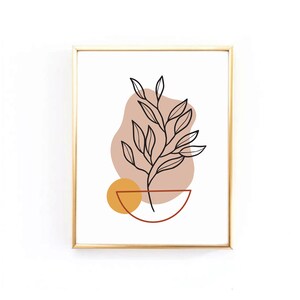 Op de afbeelding: Een minimalistische line art print van een plant met bladeren in een bruine en gele geometrische pot. De print is ingelijst in goud.