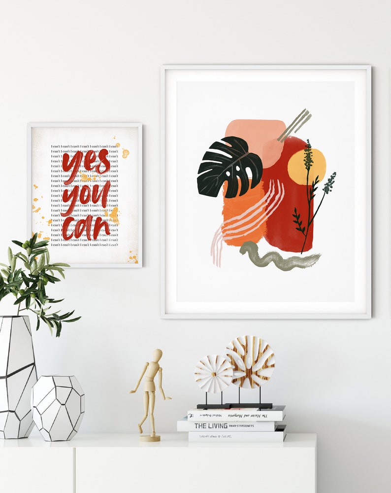 May include: Two framed prints, one with a motivational quote "yes you can" in red lettering and the other with an abstract design featuring a green leaf, orange and red brushstrokes, and a yellow sun.