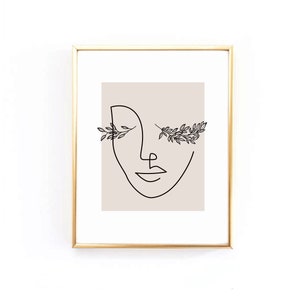 Op de afbeelding: Een zwart-witte lijntekening van een gezicht met bloemmotieven rond de ogen. De tekening is op een beige achtergrond en is ingelijst in een gouden lijst.