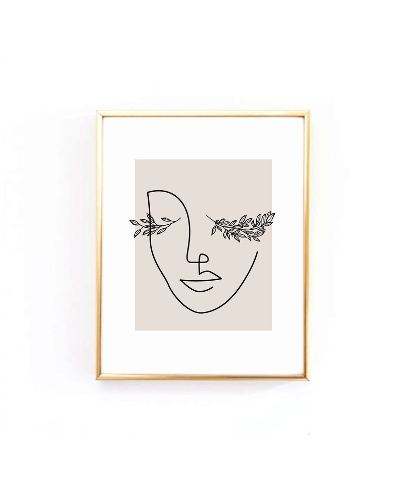 Op de afbeelding: Een zwart-witte lijntekening van een gezicht met bloemmotieven rond de ogen. De tekening is op een beige achtergrond en is ingelijst in een gouden lijst.