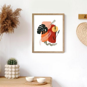 May include: Abstract art print with a red, orange, and pink color scheme. The print features a large leaf, a sun, and a few lines. The print is framed in a light wood frame.