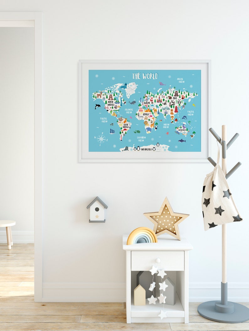 May include: A white framed world map print with colourful illustrations of animals and landmarks. The map is on a light blue background with the title "The World" at the top. The print is hanging on a white wall in a room with a white bedside table, a wooden star, and a rainbow.