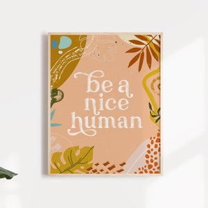 May include: A peach-colored poster with a white background and a floral design. The poster says "be a nice human" in white text.