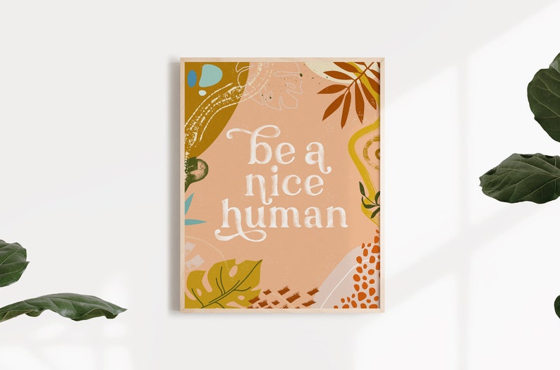 May include: A peach-colored poster with a white background and a floral design. The poster says "be a nice human" in white text.