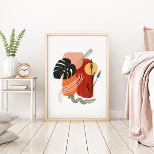 May include: Abstract art print with a large green leaf, red, orange, and pink shapes, and a yellow circle. The print is framed in a light wood frame.