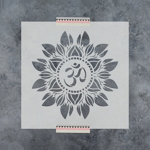 May include: A white stencil with a mandala design featuring the Om symbol in the center. The mandala is made up of intricate floral patterns.