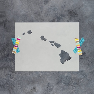 May include: A white stencil of the Hawaiian islands, taped to a gray textured surface. The stencil is shaped like the islands of Hawaii, with the main island of Hawaii being the largest.
