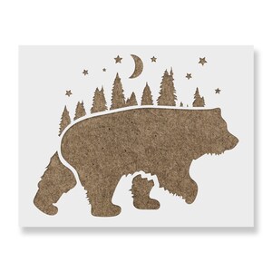 May include: A brown bear silhouette stencil with a forest, moon, and stars design. The bear is walking, with a forest of trees along its back. The moon and stars are above the trees, creating a night scene. The stencil is on a white background.