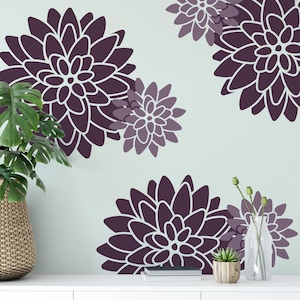 May include: A set of wall decals featuring large, stylized dahlia flowers in shades of deep purple and light lavender. The floral designs are arranged in a cluster pattern with white outlines, creating a bold graphic display on a light wall surface.