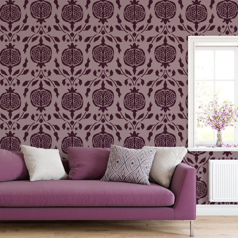 May include: A purple sofa with two white pillows and one patterned pillow sits in front of a wall with a repeating pattern of burgundy pomegranates.