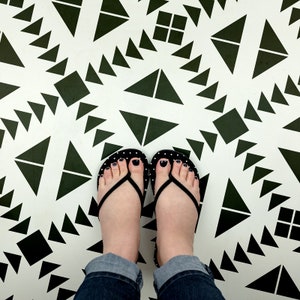 May include: A pair of black flip-flops with white polka dots on a white floor with a black and white geometric pattern.