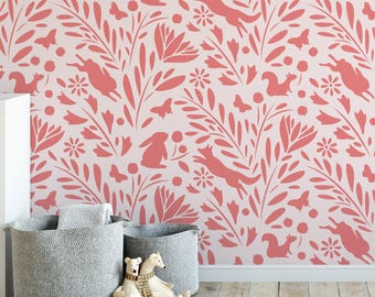 May include: Two light gray woven fabric storage baskets sit on a wooden floor in front of a wall covered in light pink wallpaper featuring a repeating pattern of coral-colored silhouettes of rabbits, squirrels, butterflies, and various flowers.