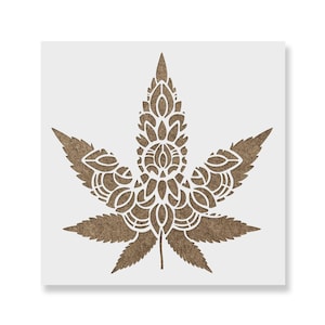 May include: A square stencil featuring a central cannabis leaf design. The leaf is composed of intricate, symmetrical white cut-out patterns layered over a textured, light brown, fiber-like material background, creating a detailed botanical motif.