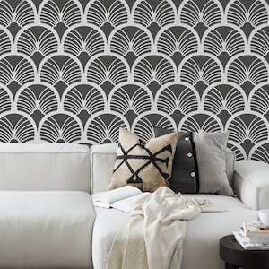 May include: A white couch with throw pillows and a blanket, set against a dark gray wall with a white geometric pattern. The pattern resembles overlapping fans or scales.