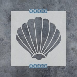May include: A square stencil featuring a centered cutout of a scallop shell with radiating ridges. The stencil is light gray with two horizontal strips of blue and white patterned tape at the top and bottom edges, set against a dark gray background.